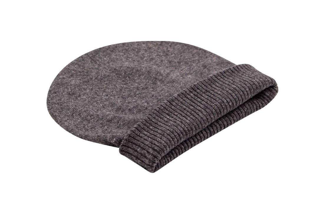 Auf dem Bild ist eine dunkelgraue, glatt gestrickte Kaschmirmütze zu sehen. Die Mütze hat einen breiten, gerippten Umschlag. Sie liegt flach auf einer weißen Oberfläche und wirkt weich sowie hochwertig verarbeitet. Die Farben und Struktur des Strickmaterials sind deutlich erkennbar. Sonstige Gegenstände oder Dekorationen sind nicht sichtbar.