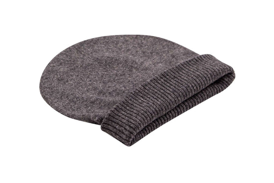 Auf dem Bild ist eine dunkelgraue, glatt gestrickte Kaschmirmütze zu sehen. Die Mütze hat einen breiten, gerippten Umschlag. Sie liegt flach auf einer weißen Oberfläche und wirkt weich sowie hochwertig verarbeitet. Die Farben und Struktur des Strickmaterials sind deutlich erkennbar. Sonstige Gegenstände oder Dekorationen sind nicht sichtbar.
