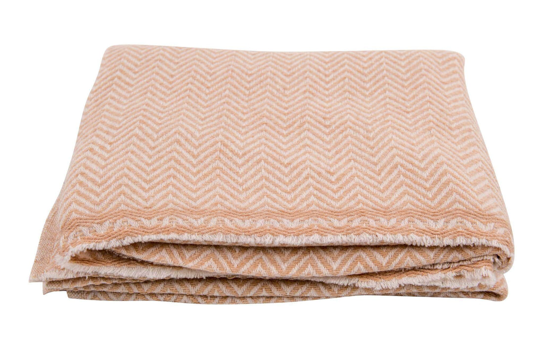 Auf dem Bild ist eine ordentlich zusammengefaltete Decke zu sehen. Die Decke hat eine goldbeige Farbe und ist mit einem markanten, durchgehenden Fischgrätenmuster versehen. Die Kanten sind leicht ausgefranst und das Material wirkt weich und flauschig. Die Decke liegt auf einer weißen, neutralen Oberfläche, der Hintergrund ist komplett weiß und ablenkungsfrei. Es sind keine weiteren Objekte oder Verzierungen zu erkennen.