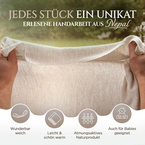 Zwei Hände halten eine beige Kaschmirdecke mit feinem Fischgrätenmuster vor unscharfem, grünlichem Hintergrund im Freien. Oben steht Text „Jedes Stück ein Unikat, erlesene Handarbeit aus Nepal“. Unten sind vier runde Symbole mit Beschreibungen: eine Feder mit „Wunderbar weich“, ein gefaltetes Tuch mit „Leicht & schön warm“, ein atmungsaktives Textil mit „Atmungsaktives Naturprodukt“ sowie ein Baby mit „Auch für Babies geeignet“. Die Decke wirkt zart, weich und hochwertig verarbeitet.